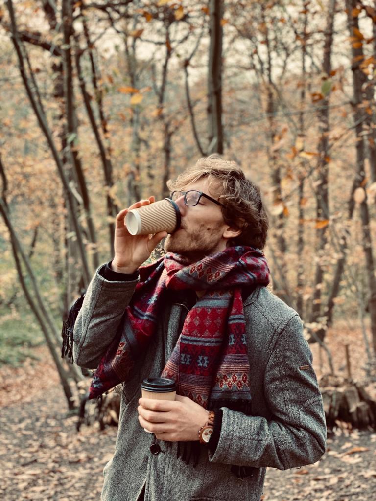 Photo of Lukas Wallrich outdoors in autumn, wearing a grey jacket and patterned scarf.